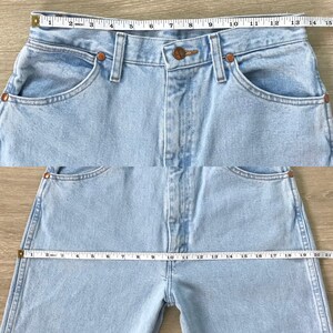 May include: Light blue denim jeans with a classic five-pocket design. The jeans are measured with a measuring tape, showing the waist and inseam. The jeans have copper-coloured rivets and a button closure.
