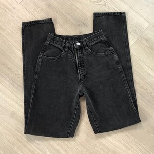 Pu&ograve; includere: Un paio di jeans neri in denim, stesi piatti. I jeans hanno una vita alta, chiusura con bottoni e un classico design a cinque tasche. Il tessuto sembra essere un denim di peso medio, con dettagli di cucitura visibili. I jeans sono di colore nero pieno.