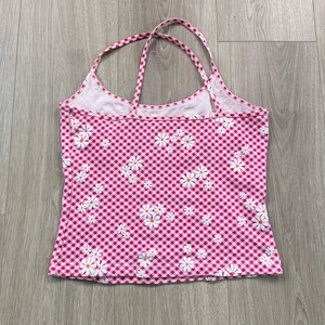 May include: Pink gingham halter top with white daisy floral pattern. The top has a scoop neckline and thin straps. The fabric is a lightweight material, ideal for summer.