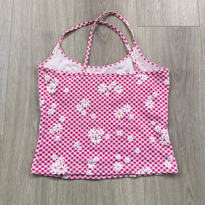 May include: Pink gingham halter top with white daisy floral pattern. The top has a scoop neckline and thin straps. The fabric is a lightweight material, ideal for summer.