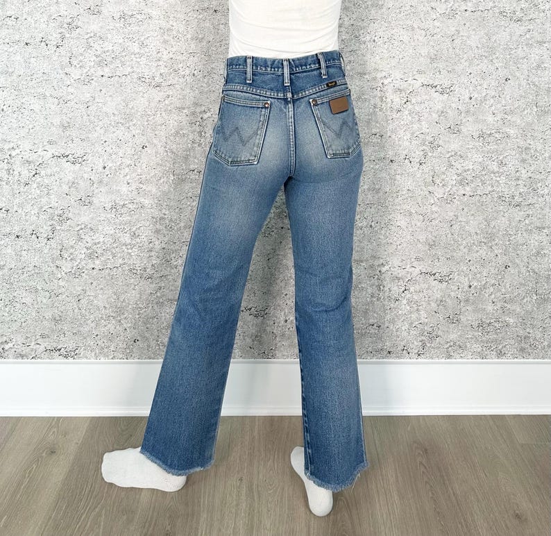 May include: Light blue denim jeans with a classic fit. The jeans feature a high waist, back pockets with a 'W' stitch design, and a brown leather patch. The jeans have a slight flare at the hem.