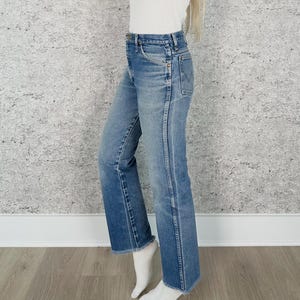 May include: Light blue denim jeans with a straight leg and a raw hem. The jeans have a classic five-pocket design and a faded wash. The model is wearing white socks.