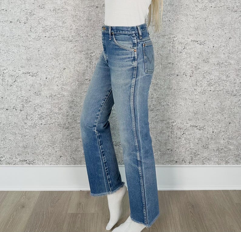 May include: Light blue denim jeans with a straight leg and a raw hem. The jeans have a classic five-pocket design and a faded wash. The model is wearing white socks.
