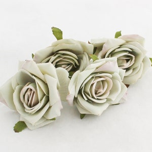 May include: Four artificial roses in a pale green color with a hint of pink in the center. The roses are arranged in a cluster and have a realistic appearance.