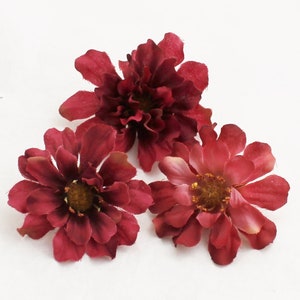 May include: Three burgundy artificial flowers with a ruffled texture. The flowers have a slightly darker center.