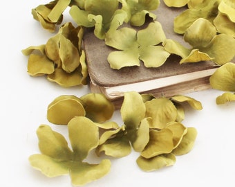 May include: A pile of green silk flower petals scattered on top of a closed book with a brown cover.