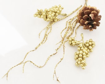 May include: Gold glitter pine cone and berry sprigs with brown stems. The pine cone is a natural brown color. The berries are clustered together and are a shiny gold color.