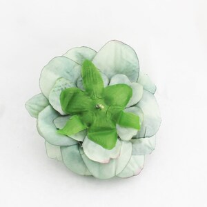 May include: A light green artificial succulent flower with layered petals and a bright green center. The flower has a small, sparkling embellishment in the center. The petals have a subtle pink hue at the edges.