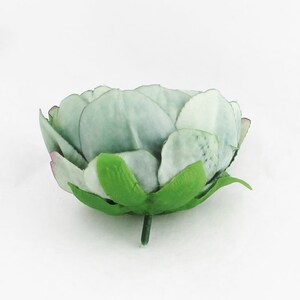 May include: A single, artificial flower head with layered petals in shades of pale green and white. The flower has a green stem and base, with hints of pink at the petal tips. The flower is likely for decorative purposes.