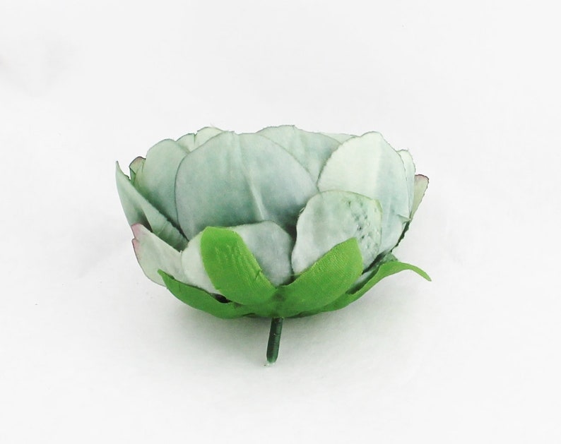 May include: A single, artificial flower head with layered petals in shades of pale green and white. The flower has a green stem and base, with hints of pink at the petal tips. The flower is likely for decorative purposes.