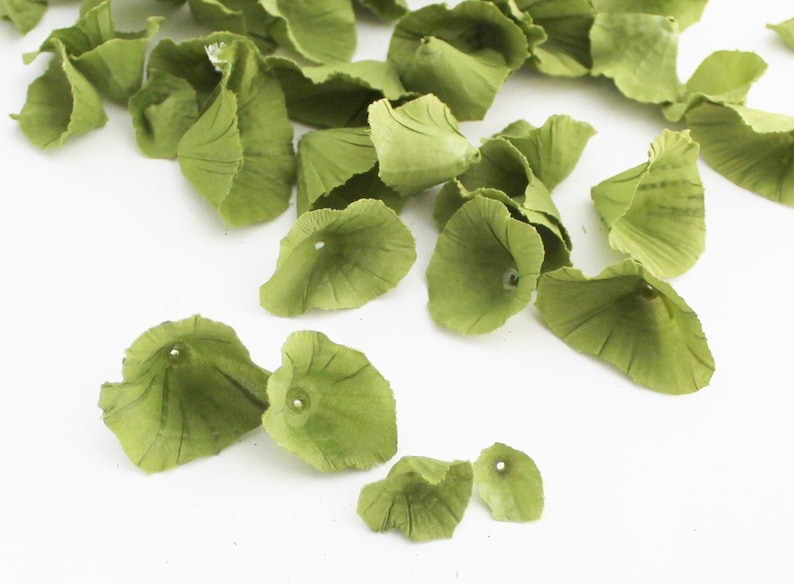 May include: Green silk flower petals with a hole in the center. The petals are scattered on a white background.