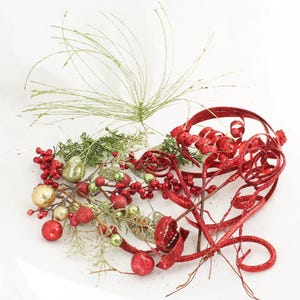 May include: Red and green Christmas decorations including sprigs of greenery, red berries, gold ornaments, and red glitter ribbon.