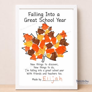 May include: A white framed print featuring the text Falling Into a Great School Year at the top, a central maple leaf outline filled with orange, yellow, and brown paper scraps, a four-line poem below, and the handwritten name Elijah.
