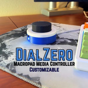 May include: A circular media controller with a black textured knob, a white top ring, and a blue base with a small glowing light. The text DIALZERO MACROPAD MEDIA CONTROLLER CUSTOMIZABLE is printed in blue and black on the image.