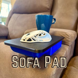 May include: A black and blue rectangular sofa pad with the text SOFA PAD printed in white. A white computer mouse with a hollow lattice shell design sits on the black surface next to a blue ceramic mug.