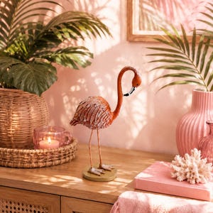 Pode incluir: Uma estatueta de flamingo em pé com um corpo texturizado de cor ferrugem e pernas longas e finas de metal. A ave tem um pescoço curvado, uma cabeça voltada para baixo com um bico preto e branco, e está montada numa pequena base circular clara.