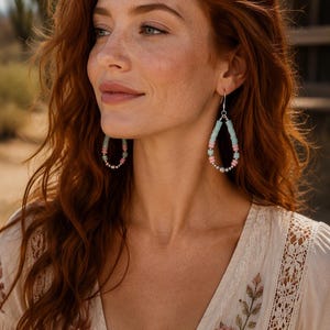 May include: Teardrop-shaped dangle earrings featuring a repeating pattern of light blue and soft pink beads, accented with small metallic silver beads at the base. The earrings are suspended from silver-toned metal hooks that secure through the ear.