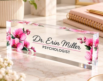 May include: A clear rectangular acrylic desk nameplate featuring a printed design of vibrant pink orchid flowers on the left and right sides. The text reads Dr. Erin Miller in a black script font with PSYCHOLOGIST in black block letters.