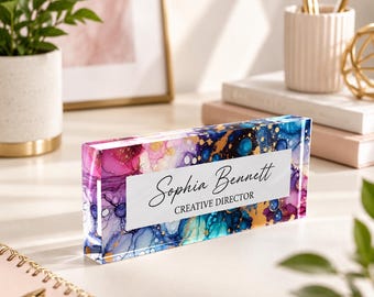 May include: A rectangular acrylic desk name plate featuring a vibrant alcohol ink pattern in shades of pink, blue, and gold. The center white rectangular label displays the black printed text Sophia Bennett and the title CREATIVE DIRECTOR.