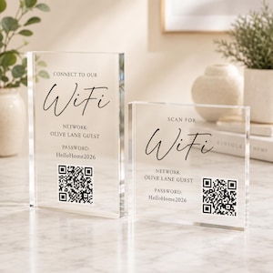 May include: Two clear acrylic rectangular signs with black text and QR codes. The left sign reads CONNECT TO OUR WiFi, NETWORK: OLIVE LANE GUEST, PASSWORD: HelloHome2026. The right sign reads SCAN FOR WiFi, NETWORK: OLIVE LANE GUEST, PASSWORD: HelloHome2026.