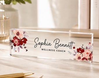 May include: A rectangular clear acrylic desk name plate featuring a floral design with deep red and soft pink flowers on the left and right sides. The text Sophia Bennett is printed in black script, with the words WELLNESS COACH below in black.
