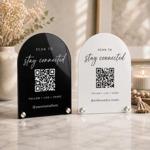 May include: Two arched acrylic signs, one black and one white, featuring the text SCAN TO stay connected, a QR code, the words FOLLOW LIKE SHARE, and social media handles. Each sign is supported by two small silver metal circular standoffs.