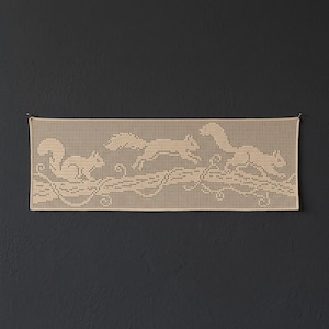 May include: A rectangular beige crochet lace panel featuring a repeating pattern of three squirrels positioned along a horizontal tree branch. The intricate needlework creates a grid-like texture, showcasing the silhouettes of the squirrels.
