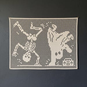 May include: A rectangular off-white crochet wall hanging featuring a grid-based pattern. The design depicts a skeleton performing a handstand on the left and a ghost dancing next to a boombox on the right, created with openwork stitches.