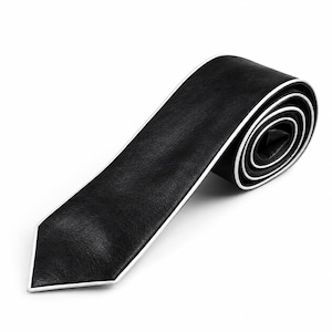 Pode incluir: Uma gravata preta com superfície texturizada e uma borda branca nítida. A gravata está enrolada em forma de espiral, destacando o contraste entre o material escuro e o acabamento branco brilhante ao longo de toda a extensão da ponta.
