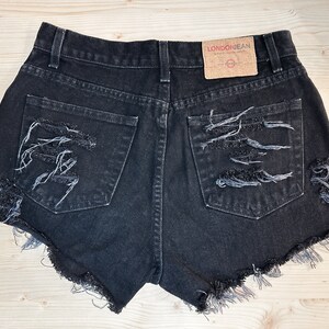 May include: Black denim shorts with distressed detailing and frayed edges. The shorts feature two back pockets and a high waist. A brown tag with the text "LONDON JEAN" is visible on the back.