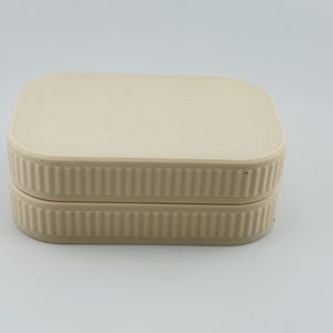 May include: A rectangular, cream-colored storage box with rounded corners and a flat lid. The sides of the box and the lid feature a consistent vertical ribbed texture, creating a uniform appearance across the entire exterior of the container.