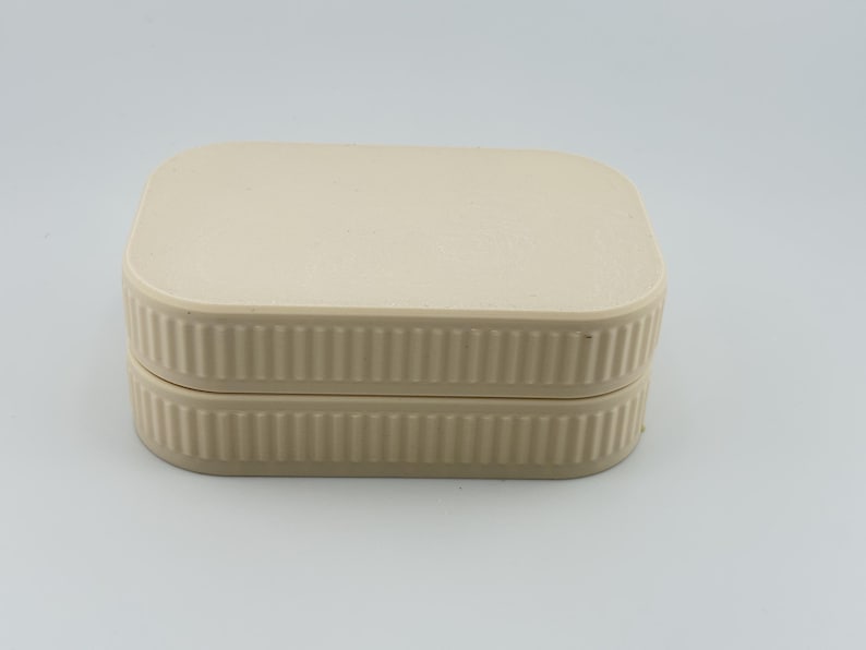 May include: A rectangular, cream-colored storage box with rounded corners and a flat lid. The sides of the box and the lid feature a consistent vertical ribbed texture, creating a uniform appearance across the entire exterior of the container.