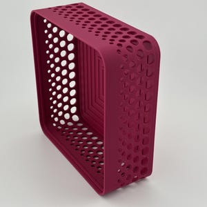 May include: A rectangular storage basket in a deep magenta color featuring a perforated pattern of circular cutouts along the sides and a stepped, square-shaped design on the interior base. The basket has rounded corners and a solid, smooth rim.