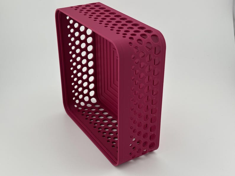 May include: A rectangular storage basket in a deep magenta color featuring a perforated pattern of circular cutouts along the sides and a stepped, square-shaped design on the interior base. The basket has rounded corners and a solid, smooth rim.