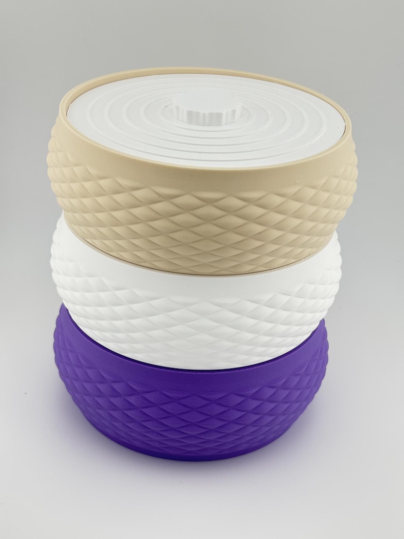 Puede incluir: Una pila de tres recipientes redondos con tapa, que presentan un patr&oacute;n de diamantes texturizado en los lados. El recipiente superior es beige, el del medio es blanco y el inferior es morado. Cada tapa tiene un dise&ntilde;o circular blanco.