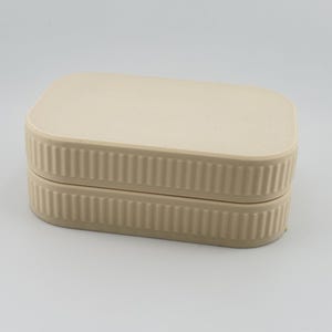 May include: A rectangular beige storage box with rounded corners and a flat lid. The sides of both the lid and the base feature a vertical ribbed texture, creating a consistent pattern around the entire perimeter of the container.