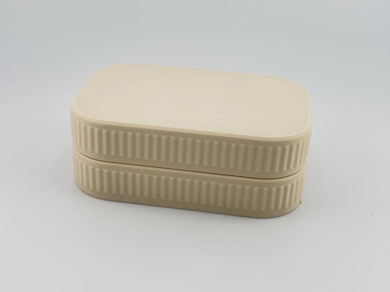 May include: A rectangular beige storage box with rounded corners and a flat lid. The sides of both the lid and the base feature a vertical ribbed texture, creating a consistent pattern around the entire perimeter of the container.