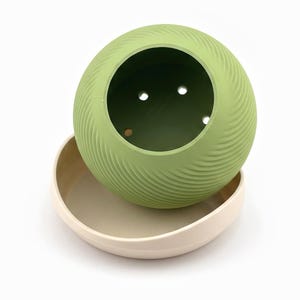 Planter tilted above its saucer showing the drainage holes in the dark green inner floor