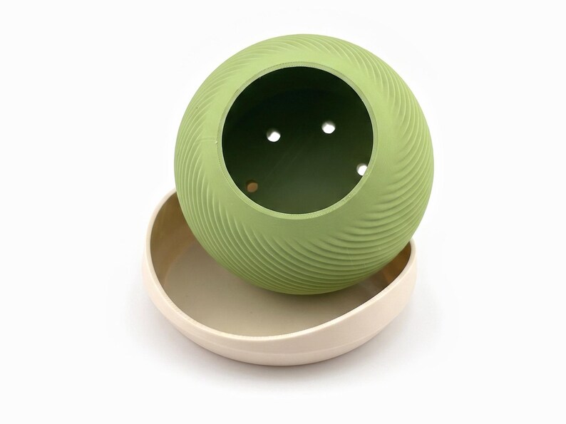 Planter tilted above its saucer showing the drainage holes in the dark green inner floor