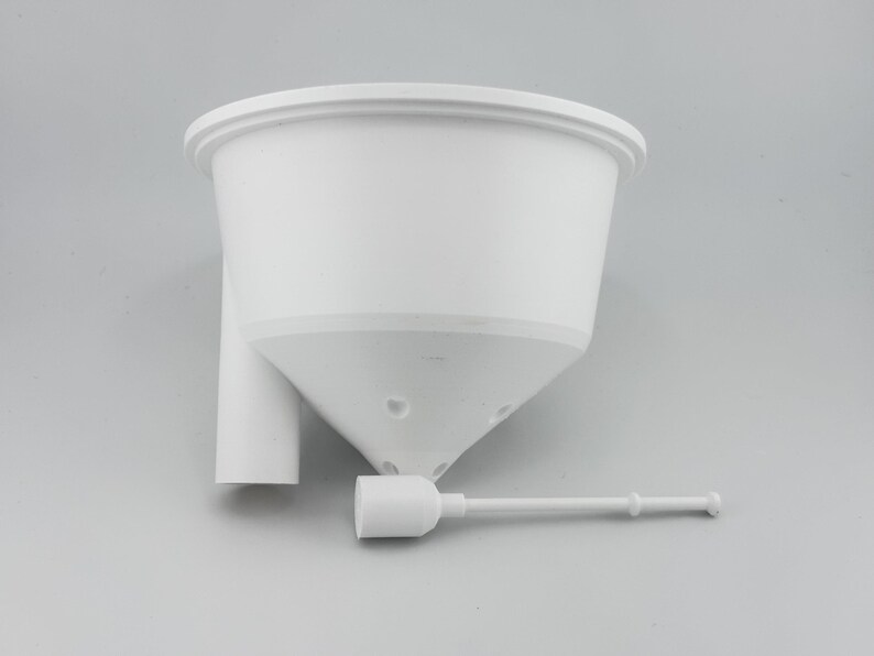 The white soil insert seen from the side, showing its cone shaped underside and the tube that runs down into the reservoir, with the separate white float stick lying in front of it.