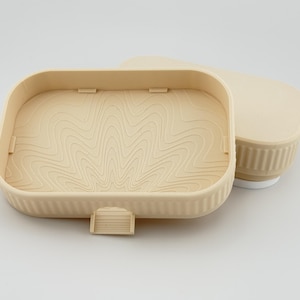 May include: A beige rectangular plastic container with a ribbed exterior and a matching lid. The interior base features a raised topographic line pattern. A small rectangular tab extends from the front edge of the container base.