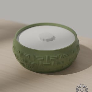 Matcha green storage bowl with a woven basket texture and a white drop-in lid, on a sunlit wooden table. 3D-rendered visualization of the exact print file.