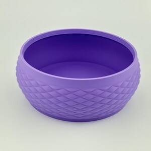 Puede incluir: Un cuenco redondo de color morado con un exterior texturizado que presenta un patr&oacute;n repetitivo en forma de diamante. El cuenco tiene una superficie interior lisa y plana y una abertura ancha, con un acabado mate uniforme en el exterior.