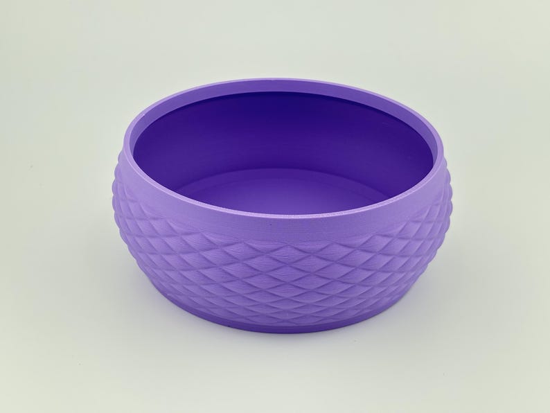 Puede incluir: Un cuenco redondo de color morado con un exterior texturizado que presenta un patr&oacute;n repetitivo en forma de diamante. El cuenco tiene una superficie interior lisa y plana y una abertura ancha, con un acabado mate uniforme en el exterior.
