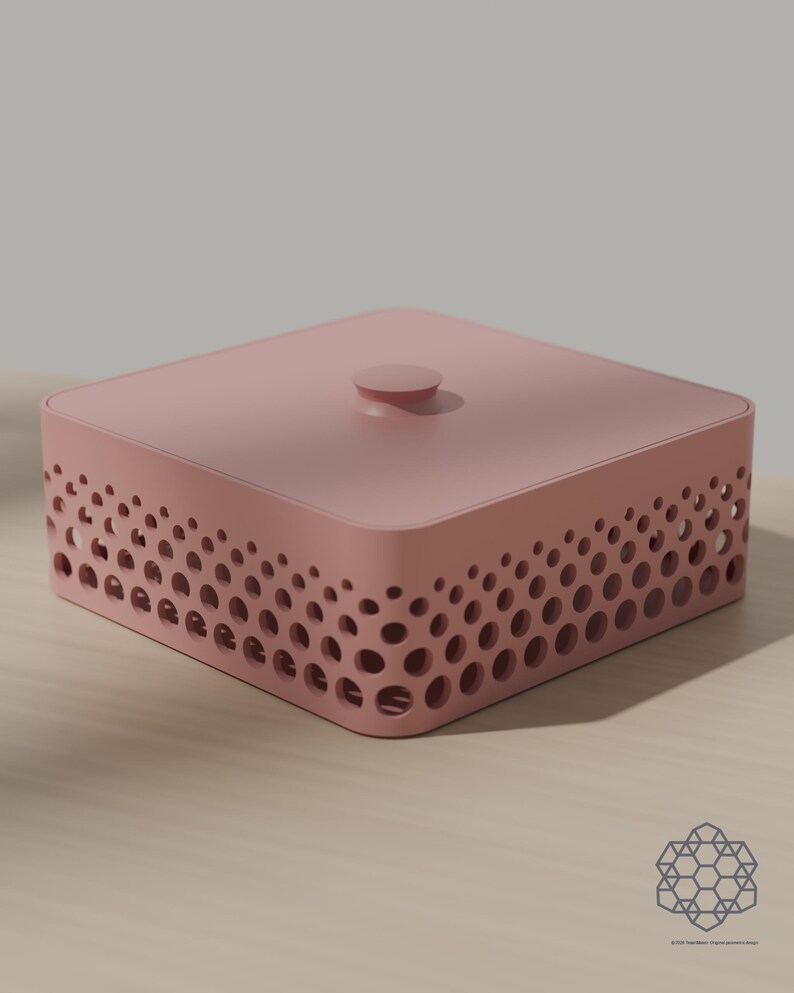 May include: A square, dusty pink storage box with a lid featuring a central circular knob. The sides of the box are decorated with a perforated pattern of varying circular cutouts that create a gradient effect along the perimeter of the container.