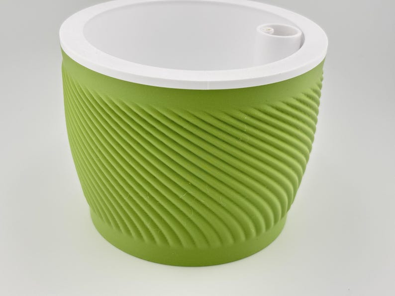 Matcha green self watering planter with a spiral ridged wall, the white soil insert seated on top and a round fill opening in its rim, photographed on a plain pale grey background.