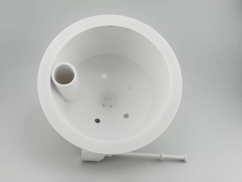 Angled view down into the white insert, with the raised fill tube opening set into the inner wall, small drainage holes across the floor, and the white float stick resting behind it.