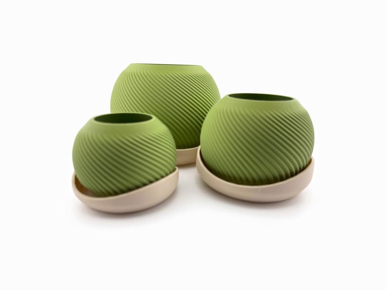 Angled group of three round matcha planters with diagonal spiral fins, each seated in a tilted cream drip saucer