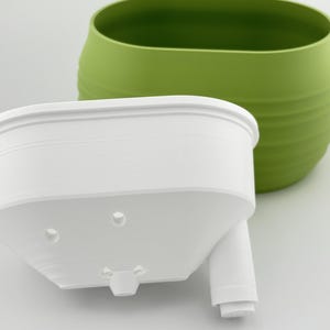 The Aquaoval's two parts side by side: the matcha green outer vessel and the white soil insert, showing the fill tube and the insert's underside.