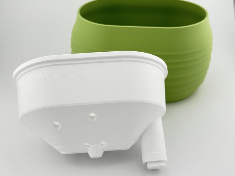 The Aquaoval's two parts side by side: the matcha green outer vessel and the white soil insert, showing the fill tube and the insert's underside.